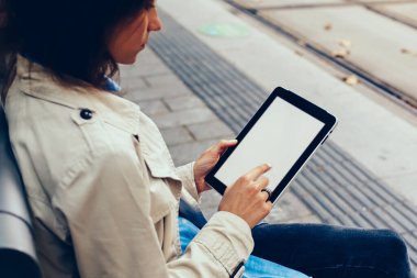 Şık giyimli genç kadın sahte ekranı modern dokunmatik yüzey üzerinde parmak ile dokunmadan yan görünüm bağlı 4 g için taşıma tramvay durağı üzerinde oturup beklerken online alışveriş yaparken Internet