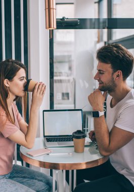 Düşünceli bir kadın, iş yerine ara verip kahve içerken iş arkadaşıyla birlikte gün ışığında kafeteryada oturup kahve içiyor.