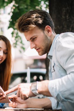 Akıllı telefon tutan neşeli, genç ve çekici bir kadın. Ve yakışıklı bir erkek arkadaşla bilgi paylaşıyor. Cihazı işaret ediyor.