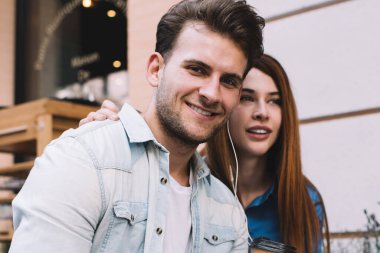 Verandada birlikte oturan mutlu çift nazikçe sarılıp, kulaklıklarla tablet kullanıyor. Nazikçe sarılıyorlar ve boş zamanlarında birlikte vakit geçiriyorlar.