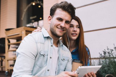 Verandada birlikte oturan mutlu çift nazikçe sarılıp, kulaklıklarla tablet kullanıyor. Nazikçe sarılıyorlar ve boş zamanlarında birlikte vakit geçiriyorlar.