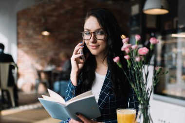 Bardaklı ve kitaplı genç bayanın telefonda konuşurken masada yemek ve vazo dolusu çiçekle oturup kameraya bakmasına sevindim.