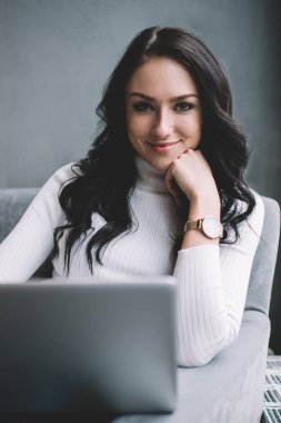 Kıvırcık siyah saçlı neşeli bir kadın işçi, modaya uygun balıkçı yaka kazaklı. Bilgisayardan finansal haberler hakkında mesajlar okuyor, kameraya bakıyor.