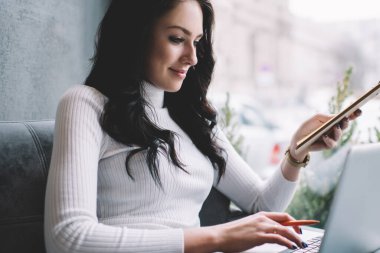 Gülümseyen kadın serbest kıyafetli rahat koltukta elinde panoyla rahatça takılıyor ve uzaktan bilgisayarını karıştırıyor.