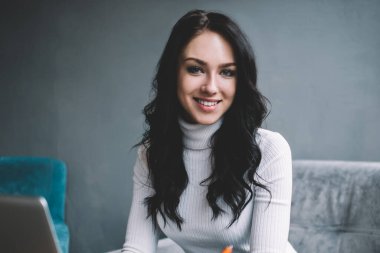 Gülümseyen kadın yönetici ofis penceresine dizüstü bilgisayarla oturmuş kameraya bakarken notlar alarak proje üzerinde çalışıyor.