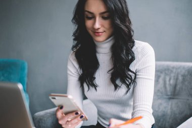 Dizüstü bilgisayarla otururken ve yaratıcı iş yerinde proje üzerinde çalışırken elinde kalemle telefonla mesajlaşan meşgul genç bayan işçiler.