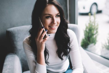 Dizüstü bilgisayar kullanan ve cep telefonuyla konuşan mutlu kadın serbest yazar yaratıcı iş yerinde oturup iş projesinde çalışıyor.