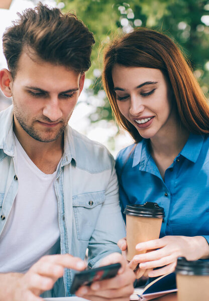 Сосредоточенный уверенный мужчина расслабляется от работы с контентом женщина показывает фото на телефоне принимая кофе напиток на открытом воздухе кафе в солнечном свете