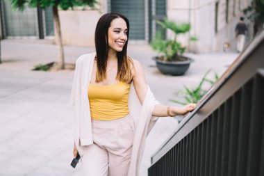 Modayı takip eden mutlu genç bayandan merdivenlerden yukarı çıkarken, parmaklıkları tutarken, gülümserken ve yüzünü çevirirken