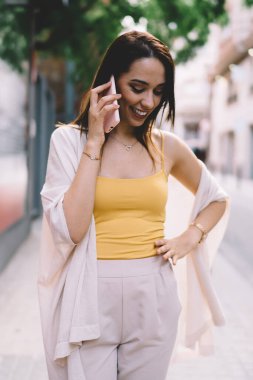 Gündüz vakti cep telefonuyla konuşurken, kadın eli belinde, şehir kaldırımında yürürken gülümsüyor.