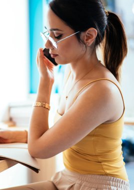 Rahat bir kafede dizüstü bilgisayar kullanarak çalışırken cep telefonundan duyulan bilgileri yazan ekin odaklı genç bayanın yan görüntüsü