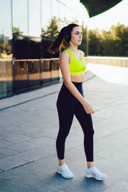 Spor elbiseli genç bir kadın ve kulaklıklı beyaz spor ayakkabılar güneşli bir günde sokakta spor yapan kulaklıklı bir kadın.