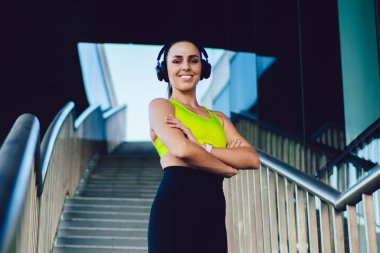 Yüzü kulaklıklı neşeli beyaz kadın koşucunun yarım boy portresi aktif fitness yaşam tarzının keyfini çıkartıyor müzik seti aksesuarında müzik dinlemekten hoşlanan mutlu profesyonel bayan sporcu.