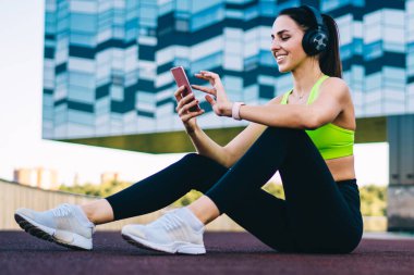 Şehir merkezinde oturan ve spor salonundaki insanlarla sabah sporu hakkında mesajlaşan mutlu formda bir antrenör. Kulaklıklı neşeli bir kadın, pozitif sesli kitap dinliyor.