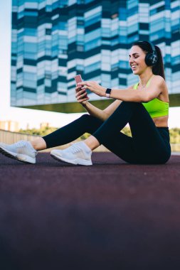 Mutlu beyaz kadın milenyum koşucusu eğitim molasında cep telefonundan komik videolara gülüyor, sağlıklı kadın blogcusu akıllı telefonu içeriği paylaşmak ve sohbet etmek için kullanıyor.