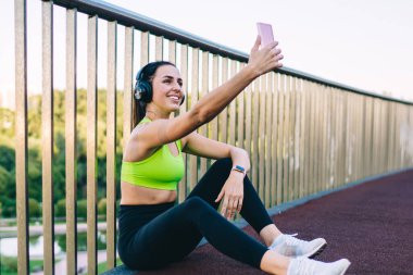 Aktif görevde olan mutlu beyaz kadın atlet, sabah antrenmanından sonra selfie çekmek için akıllı telefon kamerası kullanıyor, cep telefonlu neşeli bir kadın web vlog 'unda paylaşmak için cep telefonundan video çekiyor.