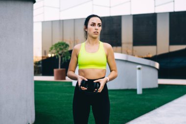 Modern binanın yanındaki kaldırımda elinde siyah kulaklıklarla şık spor kıyafetleri ve spor ayakkabıları olan zayıf aktif kadın koşucu.