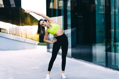 Spor giyim bölümünde genç, zayıf bir bayan eğitim sırasında şehir binasının yakınındaki bir sokakta kulaklıkla durup müzik dinliyor.