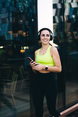 Olumlu beyaz kadın koşucu etkisinde koşucu açık havada eğitim alırken medyayı cep telefonuyla paylaşıyor, gülümseyen erkek sporcu idmanda kulaklıkla dinlemek için cep telefonundan çalma listesini seçiyor