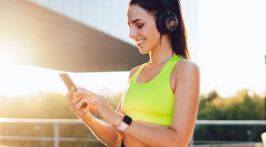 Elektronik kulaklıklı, akıllı telefon cihazıyla mobil sohbetleri kontrol eden, medya uygulamasından müzik podcast 'i seçen, modern cihazda gülümseyen kullanıcı ağı web sayfası