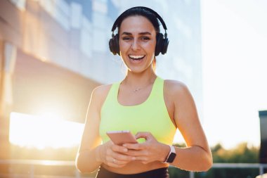 Neşeli, heyecanlı sporcu kadının yarım boy portresi sabah antremanı sonuçlarından memnun cep telefonu uygulaması, aktif spor yapan güzel kız sporcu kulaklıkla spor salonundaki spor programlarına gülüyor.