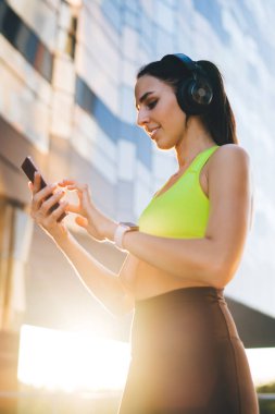 Alt taraftan, aktif giyimli genç sporcu kadının cep telefonuyla mesajlaşması ve antreman sırasında sokakta dikilirken müzik listesinden müzik dinlemesinin keyfini çıkarması.