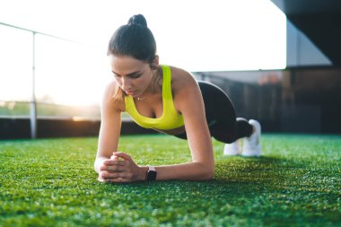 Konsantre kadın sporcu aktivite kıyafetleri içinde kalas egzersizleri yapıyor kas gücünü dışarıda çalıştırıyor, enerjik spor yapan kadın egzersiz yapıyor kilo vermek ve fiziksel güç kazanmak için çabalıyor.