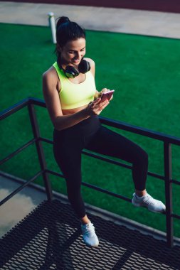 Antrenmandan sonra çevrimiçi ağ kuran mutlu kadın cep telefonu cihazı, bluetooth kulaklıklı milenyum atleti spor bloguna bağlanmak için akıllı telefonu kullanıyor.