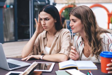 Özel ders için webinar videosu izleyen kafası karışmış kadınlar ve eğitim için düzenlenen beyin fırtınası toplantısında kaldırım kafeteryasında öğrenim gören beyaz kız öğrenciler üniversite sınavlarına hazırlanıyor.