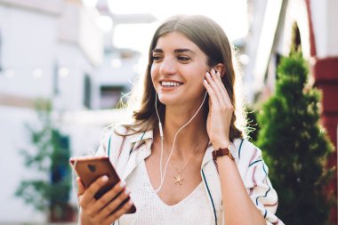 Elektronik ekipmanlı mutlu beyaz kadın iletişim numarasını arıyor, kulaklıklı neşeli hippi kız akıllı telefon uygulamasından olumlu müzik yayını dinliyor.