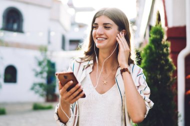 Elektronik ekipmanlı mutlu beyaz kadın iletişim numarasını arıyor, kulaklıklı neşeli hippi kız akıllı telefon uygulamasından olumlu müzik yayını dinliyor.