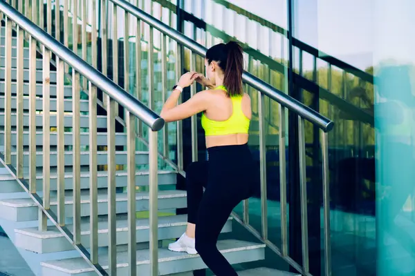 Moda eşofmanlı aktif bir bayan atletin şehir merdivenlerinde yürüyüş yaparken dışarıda fiziksel dinlenmenin tadını çıkarırken, şehirde mükemmel vücut şekli eğitimi almış güzel bir koşucu.