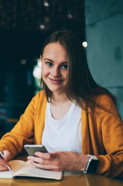 Ödev yapan başarılı kız öğrencinin portresi ve internet sitelerinden bilgi okuyan notlar almak akıllı telefon kullanan, cep telefonu tutan ve kompozisyon yazan neşeli hippi kızlar.