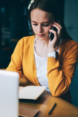 Ciddi bir kadın, modern dizüstü bilgisayarda ödeme yaparken bakiyeyi kontrol etmek için operatöre telefon ediyor. Sosyal ağlarda bilgi arayan konsantre hippi kız aynı zamanda iş arkadaşına sesleniyor.
