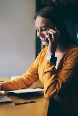 Kafeteryadaki kablosuz 4G bağlantısını kullanarak modern dizüstü bilgisayarda mesaj yazarken akıllı telefon cihazıyla arkadaşınla iletişim kuran sevimli yüzlü pozitif kadın serbest çalışan.