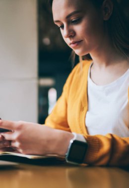 Akıllı telefondan mesaj gönderen konsantre bir kız öğrenci dizüstü bilgisayarla aynı masada oturuyor ve kafeterya kablosuz internete bağlanıyor. Ciddi bir kadın yeni telefon ihbarnamesini güncelliyor.