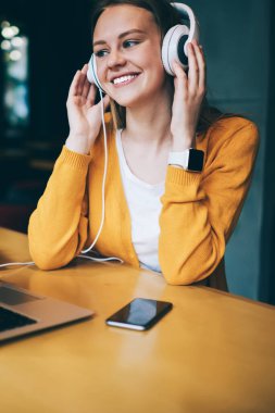 Neşeli hippi kız multimedya uygulaması ve kulaklıkla olumlu müzik listesi dinliyor, mutlu gülümseyen kadın kulaklıkla yüksek sesli favori müziğin tadını çıkarıyor ve dizüstü bilgisayarla ön tarafta oturuyor.