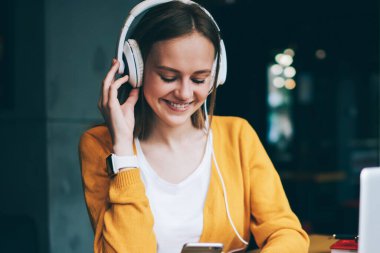 Başarılı bayan meloman mobil uygulama ile radyo istasyonunu arıyor kulaklıklardan gelen güzel seslerin keyfini çıkarıyor, cep telefonuyla mesaj yazan mutlu hippi kız medya çalma listesi dinlerken