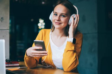 Elektronik kulaklıklı pozitif kadın melodinin portresi ilginç ses kitapları dinliyor ve sosyal ağlardaki arkadaşlarla mesajlaşıyor kafeteryadaki akıllı telefondan 4 g bedava internet kullanıyor.