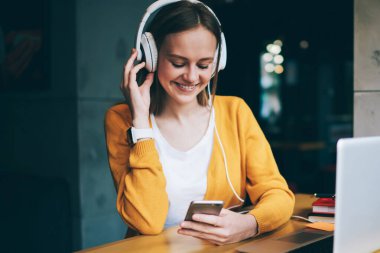 Başarılı bayan meloman mobil uygulama ile radyo istasyonunu arıyor kulaklıklardan gelen güzel seslerin keyfini çıkarıyor, cep telefonuyla mesaj yazan mutlu hippi kız medya çalma listesi dinlerken