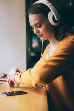 Genç bir kadın, kulaklıkla ciddi ses kitaplarını dinlerken GPS takibini ve takılabilir akıllı saatleri kontrol ediyor. Kafeteryada dizüstü bilgisayarla oturan, kulaklıklı, beyaz bir hippi kız.