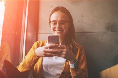 Gözlüklü neşeli hippi kız arkadaşlarıyla sohbet ettiği için heyecanlanıyor. Cep telefonunda bedava 4G internet kullanıyor. Boş zamanlarında medya uygulaması aracılığıyla video izleyen mutlu bir kadın.