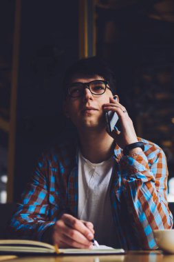 Cep telefonuyla müşterilerle konuşan ve not defterine bazı bilgiler yazan meşgul bir erkek yönetici. Modern akıllı telefon aracılığıyla iletişim kuran düşünceli gözlüklü öğrenci masaüstünde oturuyor ve mesaj kaydediyor.