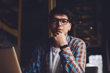 Optik gözlüklü zeki öğrencilerin portresi kameraya bakıyor kitaplara bakıyor ve hızlı internet bağlantısı olan modern bilgisayarlara bakıyor. Kafenin içinde serbest çalışan erkek metin yazarı.