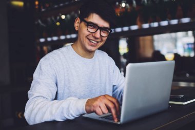 Modern dizüstü bilgisayarda çalışan ve kameraya bakıp gülümseyen 4G yüksek hızlı internet bağlantısı kullanan şık gözlüklü profesyonelin portresi