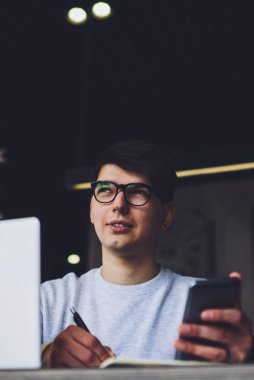 ?Gözlüklü, elinde akıllı telefonla not defterine mesaj yazan yakışıklı bir adam. Ev ödevi hakkında düşünen düşünceli bir öğrenci dizüstü bilgisayarın başında oturup bazı bilgileri not alıyor.