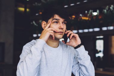 Modern akıllı telefondan konuşan ve çözümü düşünen meşgul genç girişimci. Kafede ders kitabıyla ahşap masada oturan düşünceli öğrenci ciddi cep telefonu konuşmaları yapıyor.