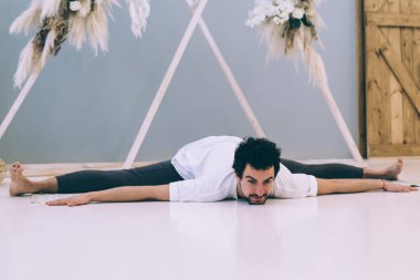 Aktif giyimli çıplak ayaklı erkek sporcu, hafif stüdyoda yoga yaparken yerde egzersiz yapıyor.