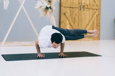 Çağdaş stüdyoda spor minderinde yoga yaparken iki ayaklı Sage Koundinya pozu veren çıplak ayaklı bir adam.