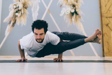 Konsantre olmuş bir adam spor minderinde sekiz açılı poziyon veriyor böylece modern stüdyoda yoga eğitimi sırasında kol ve bacak merkezini ve bilekleri güçlendiriyor.